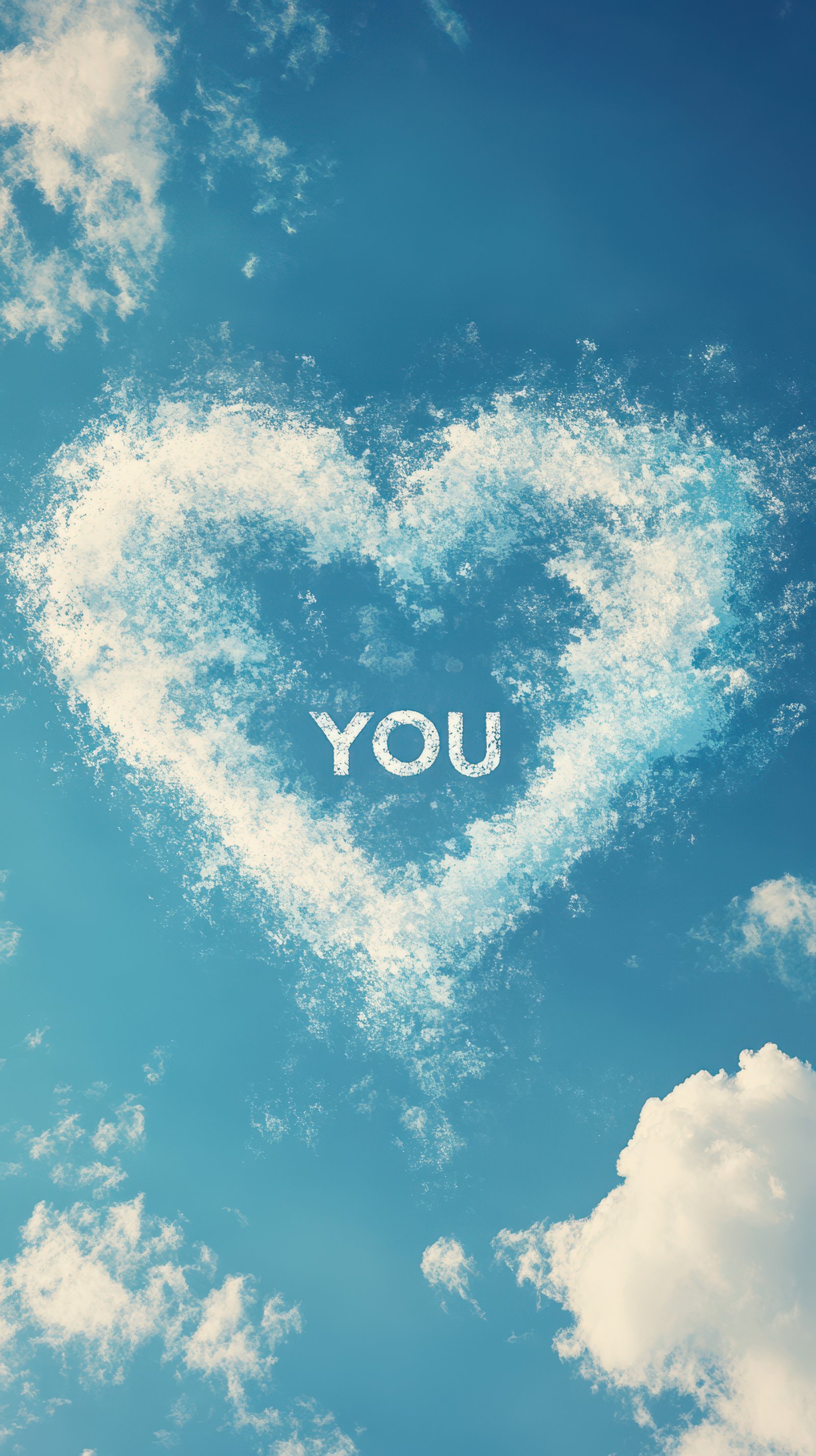 Clouds form a heart shape with the word you written in clear sky above white fluffy clouds